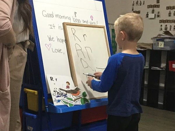A young learner practising the letter R on a whiteboard alongside an educator